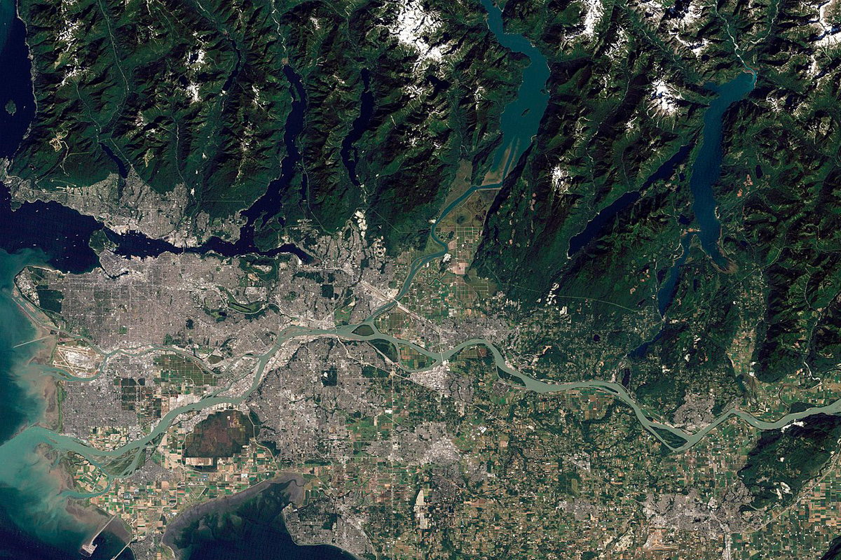 Aerial view of a sprawling urban area with winding rivers, surrounded by mountainous terrain and water bodies, where an expert arborist tends to the lush greenery dotting the landscape.